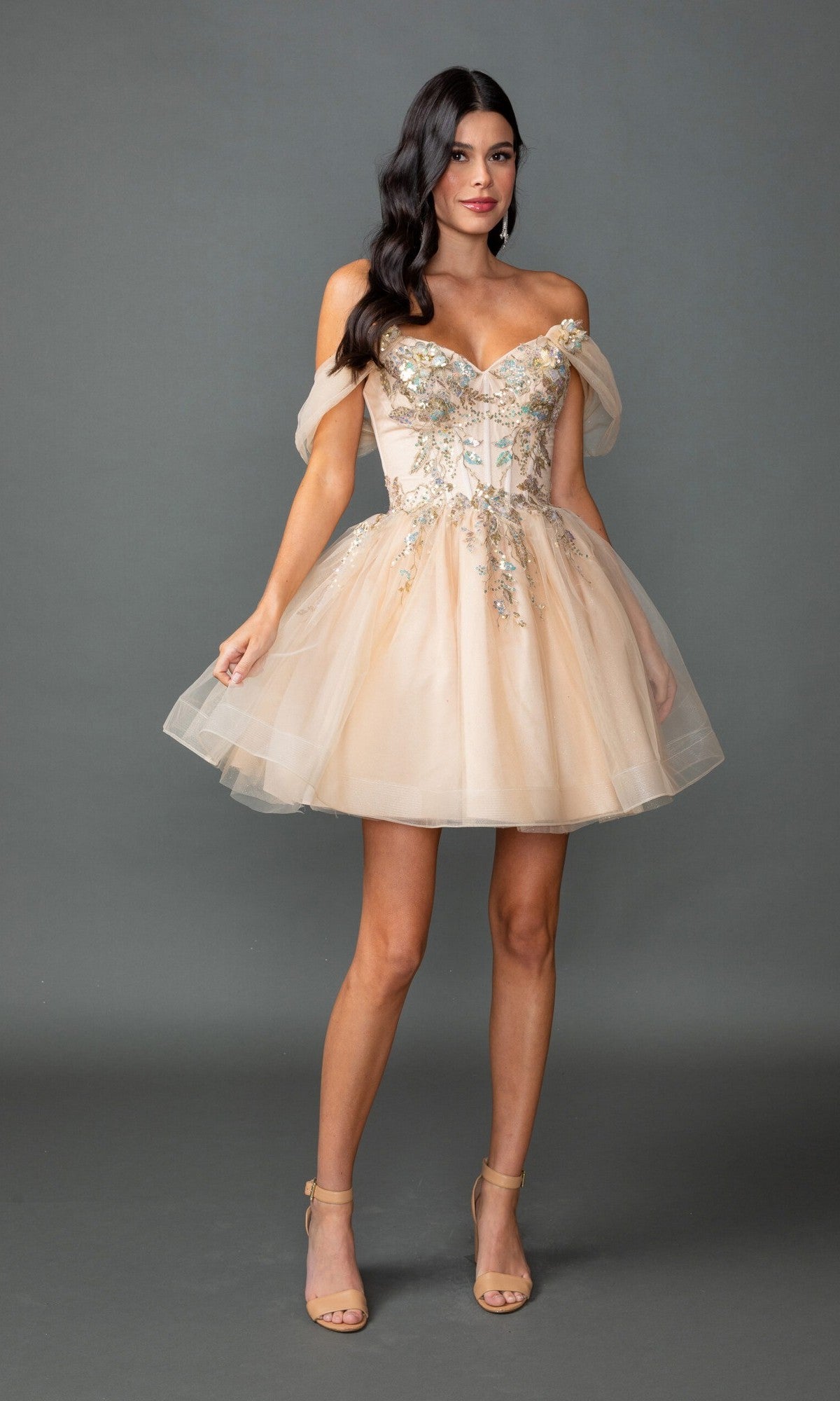 A woman models the Dancing Queen 3423 short prom dress, featuring an off-the-shoulder blush tulle A-line skirt with delicate beaded embroidery, against a plain gray background.